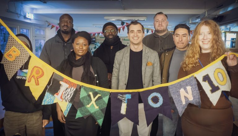 A group of people hold up homemade bunting that reads "BRIXTON" in The Remakery.