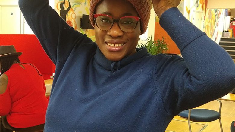 Woman smiling to camera holding a box above her head.